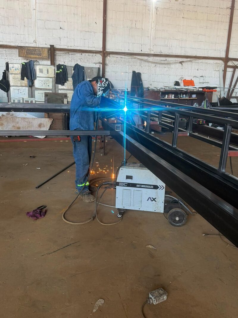 A welder joining a trailer frame on our shop floor, arc lit